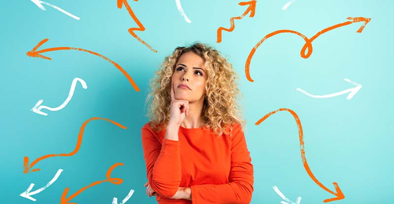Currency of Education and Challenge Exams A photo featuring a blue background with a Caucasian woman wearing an orange shirt, looking up thoughtfully. Squiggly arrows in orange and white point away from her, symbolizing ideas or decision-making.