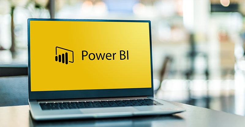 A sneak peek into the Power (of) BI & DAIS A photo of a laptop open and placed on top of a table and it reads, "Power BI".