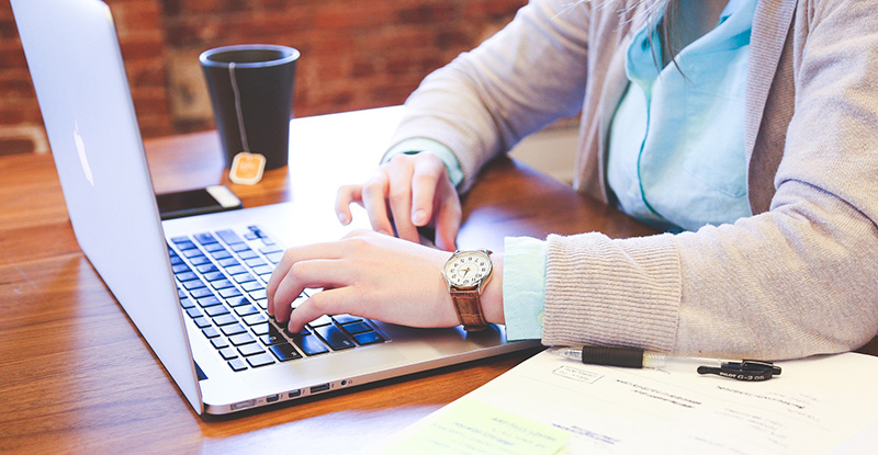 The Transcript Reassessment Process A photo of a woman typing on a laptop with a notebook on one side and a tea mug on the other.