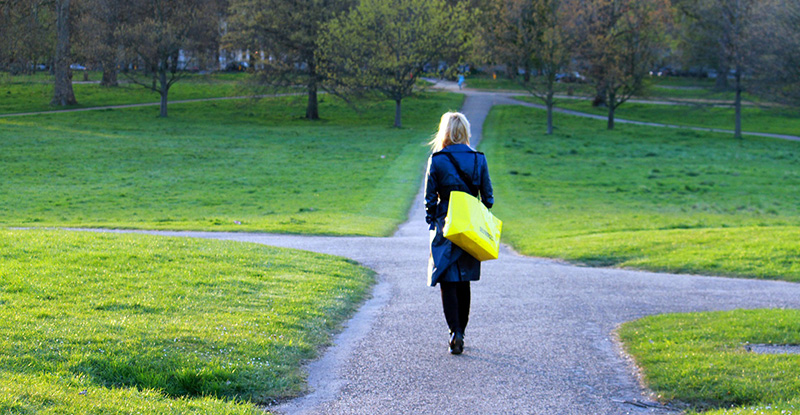 A photo of a woman with a yellow bag walking in a park.