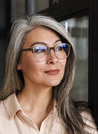 A white-haired Asian woman with spectacles looking away while posing for the camera.
