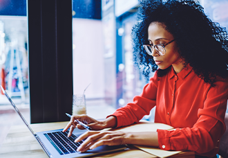 An African American woman waring a red blouse is typing on a laptop.