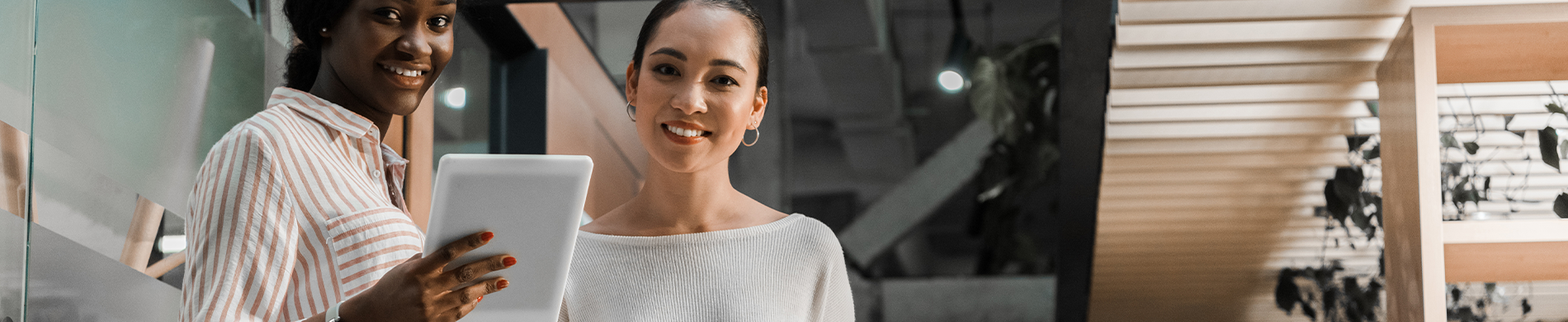 A banner image of an African woman holding a tablet and an Asian woman standing beside her, both smiling at the camera.