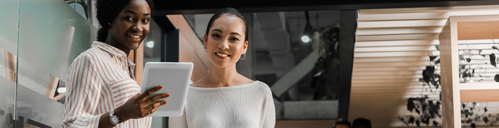 A banner image of an African woman holding a tablet and an Asian woman standing beside her, both smiling at the camera.