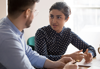 An Indian woman talking to a Caucasian man in an office setting, engaged in conversation.