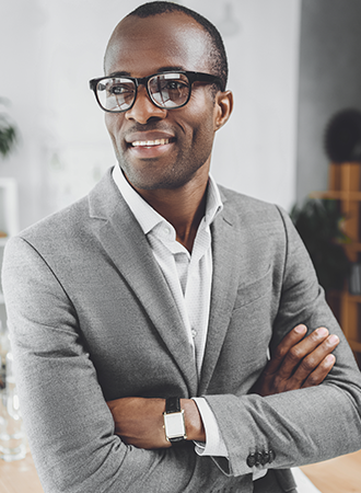 An African man wearing a grey suite with glasses is posing for the camera while looking away.
