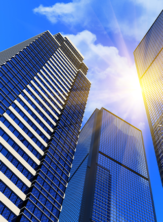 A photo taken from the bottom up, capturing tall glass buildings reflecting the blue sky, with sunlight shining through and creating a radiant effect.